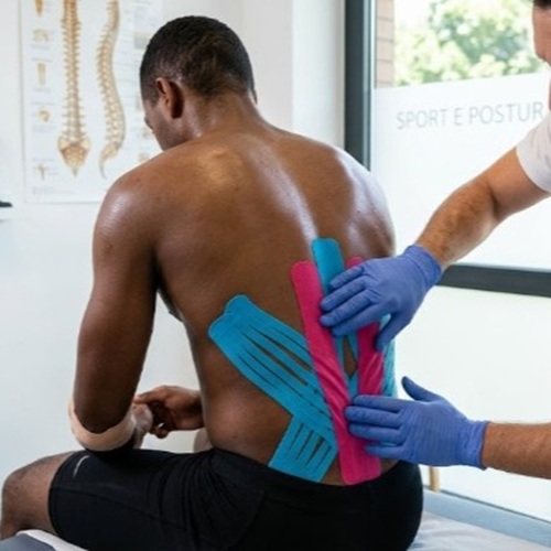 Specialista in posturologia applica bande di kinesiotaping neuromuscolare sulla schiena di un atleta.